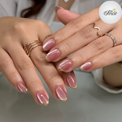 Close-up of a person's hands displaying short, oval-shaped nails with a shimmery pink cat-eye polish and delicate gold outlines.