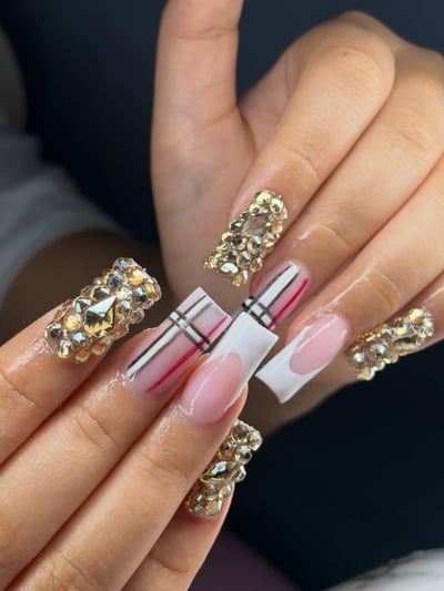 Close-up of long, square-shaped nails featuring a mix of clear and gold rhinestones, pink and black plaid patterns, and classic white French tips.