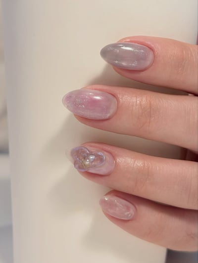 Oval, medium-length nails with a translucent pastel purple and pink aurora design, featuring a 3D heart charm.