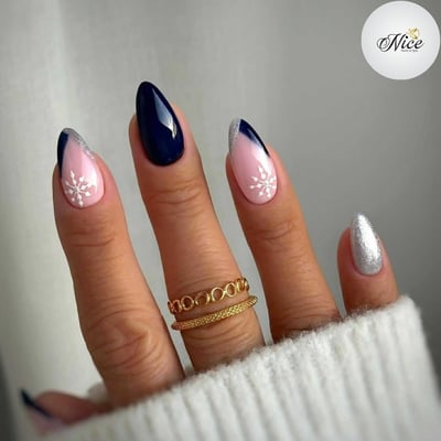 Almond-shaped nails featuring a winter design with glossy navy, light pink, silver glitter, and white snowflakes on a medium skin tone hand.