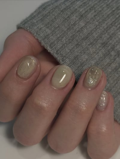 Oval, medium-length nails with a translucent pale green polish, featuring silver glitter on the ring and pinky fingers.