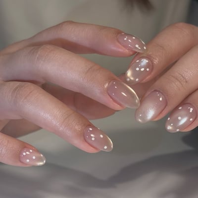 Medium almond nails with a translucent nude cat-eye base and white polka dot accents.