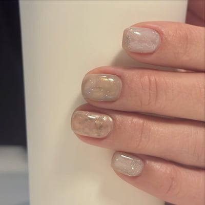 Oval nails with a translucent pastel base, featuring gold shimmer, silver glitter, and gold foil accents.