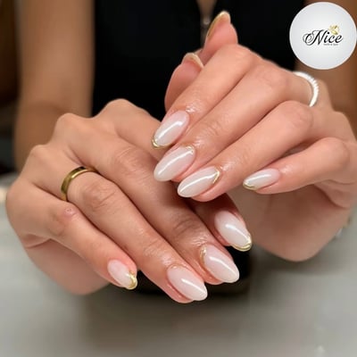Close-up of two hands showcasing elegant oval nails with a sheer milky base and delicate gold metallic outlines.
