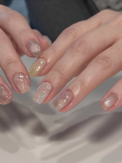 Medium square nails with a translucent nude base, aurora shimmer, and gold and silver glitter accents.