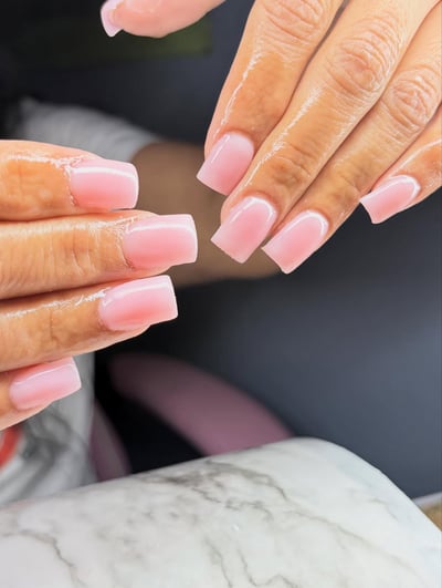 Close-up of hands with medium skin tone showcasing perfectly manicured, glossy, translucent baby pink square-shaped nails.