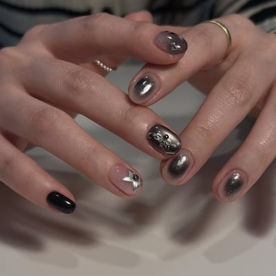 Oval nails with a mix of metallic silver ombre, solid black, and a nude base with a silver star and black stud.