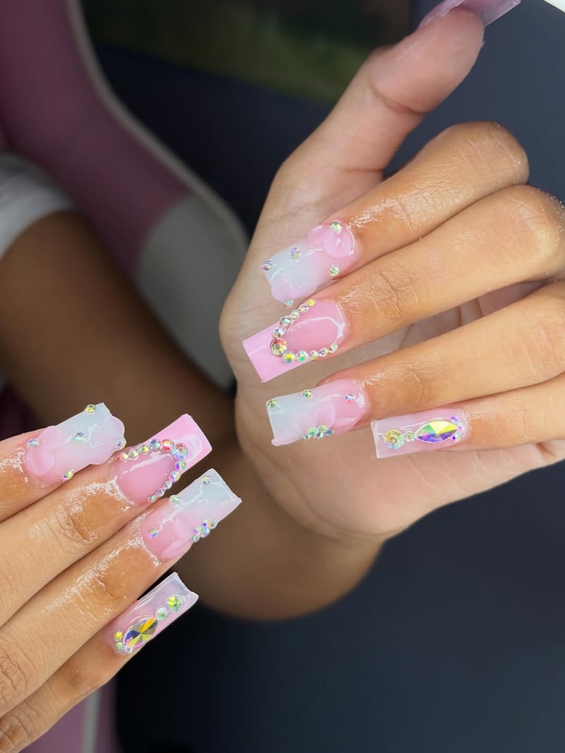 Close-up of long, sculpted coffin-shaped nails featuring a pink and white ombre, lavishly adorned with iridescent rhinestones in heart shapes and clusters.
