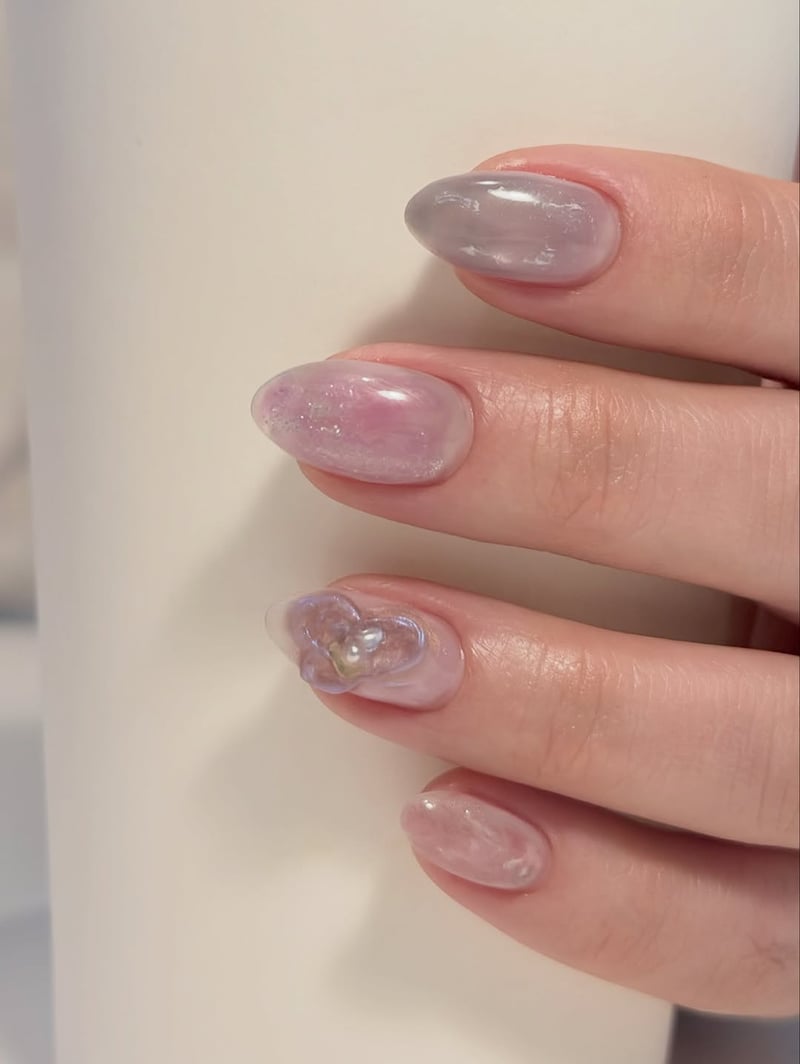 Oval, medium-length nails with a translucent pastel purple and pink aurora design, featuring a 3D heart charm.