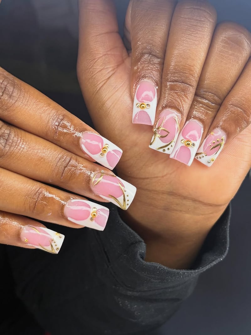 Elegant square-shaped nails featuring a pink and white base with intricate gold floral-inspired designs, accented with gold beads and clear rhinestones.