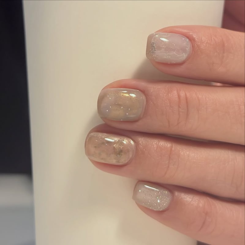 Oval nails with a translucent pastel base, featuring gold shimmer, silver glitter, and gold foil accents.