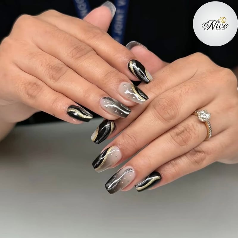 A close-up of hands showcasing glamorous black, gold, and silver coffin-shaped nails with metallic swirls and ombré effects.