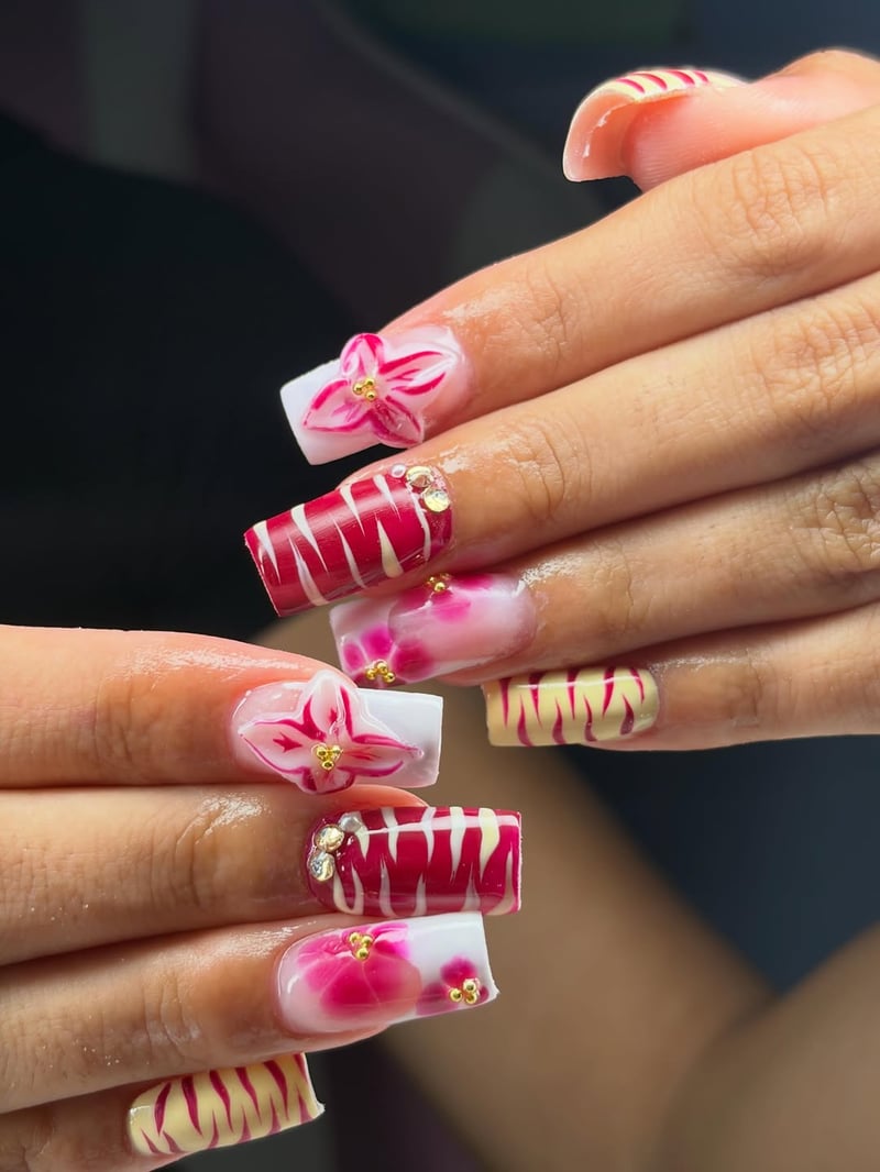 A close-up shows a hand with long, square nails featuring a festive design of red and white stripes, 3D pink flowers with gold studs, and pale yellow tiger-stri