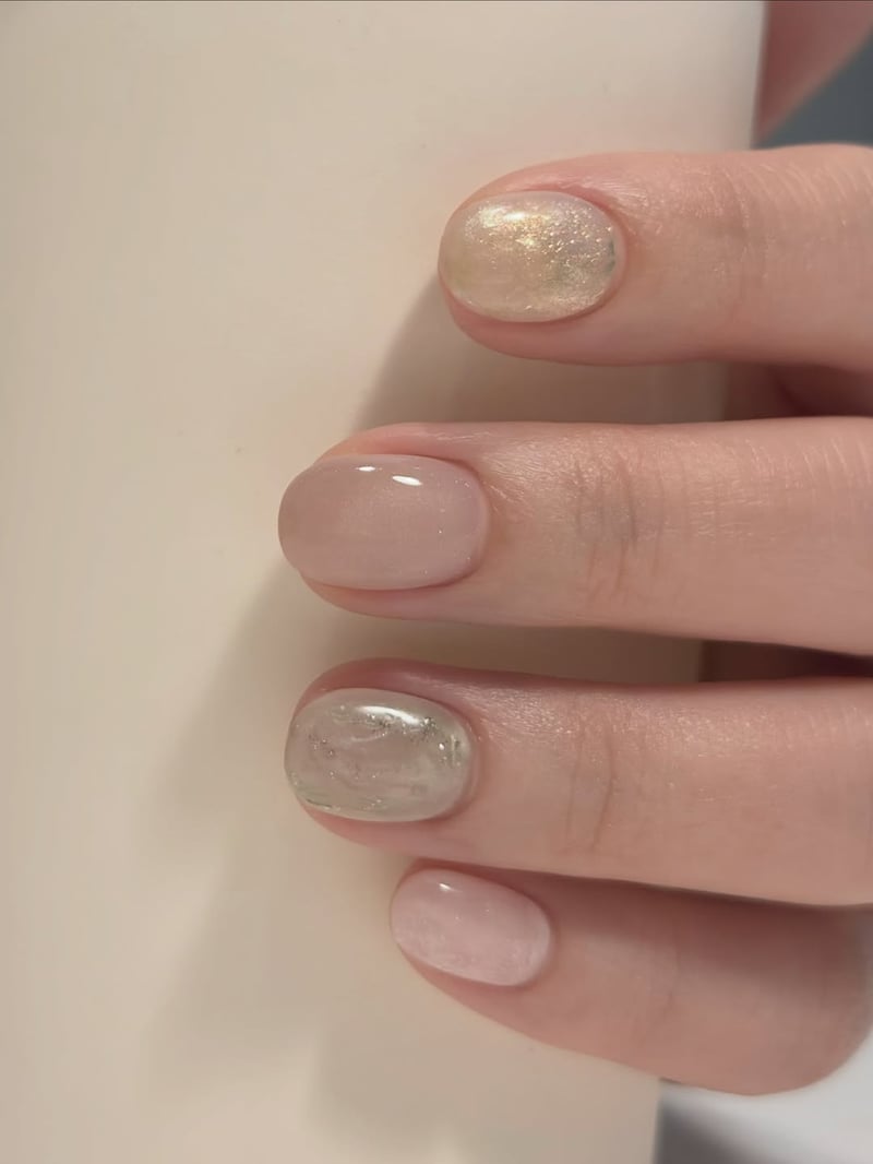 Short oval nails feature a mix of sheer pink and shimmery marble designs with gold and green accents.