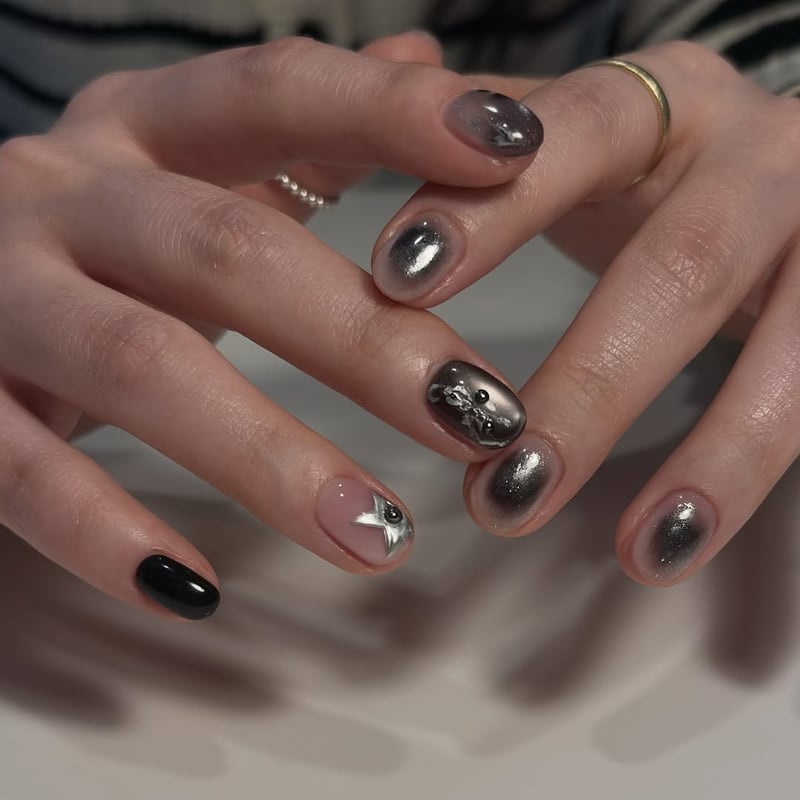 Oval nails with a mix of metallic silver ombre, solid black, and a nude base with a silver star and black stud.